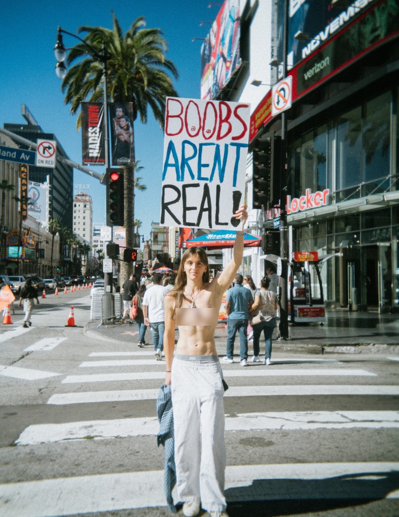 Lillian Lover holding BOOBS AREN'T REAL sign at a Hollywood crosswalk